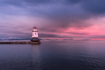 The Burlington Lighthouse before the storm under a cloudy, colorful sky at sunset. The sky is threatening. On the horizon, we can see that the clouds are low.