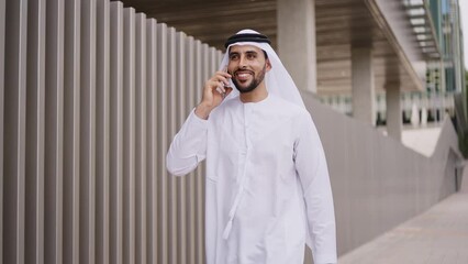 Wall Mural - Handsome businessman with the traditional emirates white outfit working outdoor in Dubai city. Concept about middle eastern cultures and business