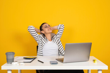 Wall Mural - Young caucasian business woman sit work at white office desk with laptop hold hands behind neck, resting. Looking aside smiling. Isolated yellow studio background. Modern office day happy employee.