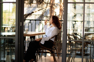 Portrait of pretty young woman sitting at table with glass of red wine using mobile phone live on social media, for business, writing stories, taking selfies and blogs at restaurant with dark interior