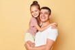 © sementsova321 - Positive optimistic father and daughter wearing casual t-shirts standing isolated over beige background dad holding child looking at camera family day.