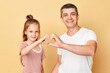 © sementsova321 - Charming positive family father and daughter wearing casual t-shirts standing isolated over beige background making heart shape love symbol together with hands.