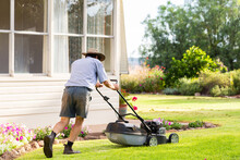 Middle Aged Australian Man Pushing Lawn Mower Mowing Grass Of House Front Yard