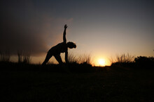 Silhouette Shot Of A Young Woman Doing Exercise On A Field With Grass Under The Sun Set Light