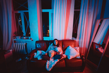 Beautiful young girl watching movie at home in a dark room with a popcorn bucket playing with her dog and sits in front of a monitor or TV.