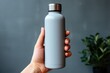 The hand is holding a tumbler thermos bottle for a mockup. steel thermos water bottle. plant decoration as the background.