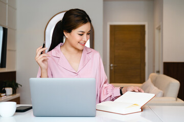 Canvas Print - Asian female entrepreneur working remotely from home office using modern computer.Young cheery happy positive cute beautiful business woman sit in home office using laptop computer...