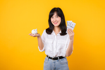 Poster - Portrait beautiful young business asian woman wearing white shirt and denim jean with a lot of cash money and piggy bank isolated on yellow background. Wealth money saving, finance investment concept.