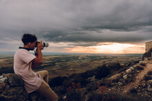 Unrecognizable Man With Camera Taking Picture Of The Sunset Evening Orange Sky With Black Clouds