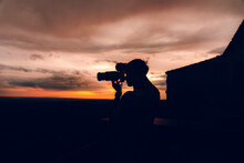 Unrecognizable Man With Camera Taking Picture Of The Evening Orange Sky With Black Clouds