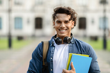 Wall Mural - Smiling Young Male Student With Workbooks And Backpack Standing Outdoors