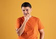© Prostock-studio - Pensive young brazilian man looking at camera with interest, dreamy guy touching chin and smiling, orange background