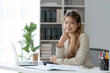 © amnaj - Confident Asian Businesswoman Sitting in Modern Office With Laptop Computer.