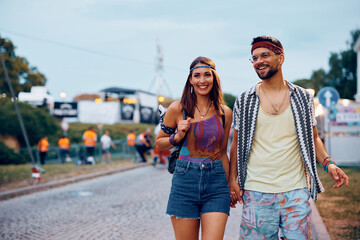 Happy couple of festivalgoers holding hands while going on open air concert.