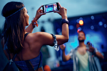 Wall Mural - Young woman photographing her boyfriend with cell phone at summer music festival.