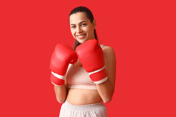 Poster - Young woman with boxing gloves on red background