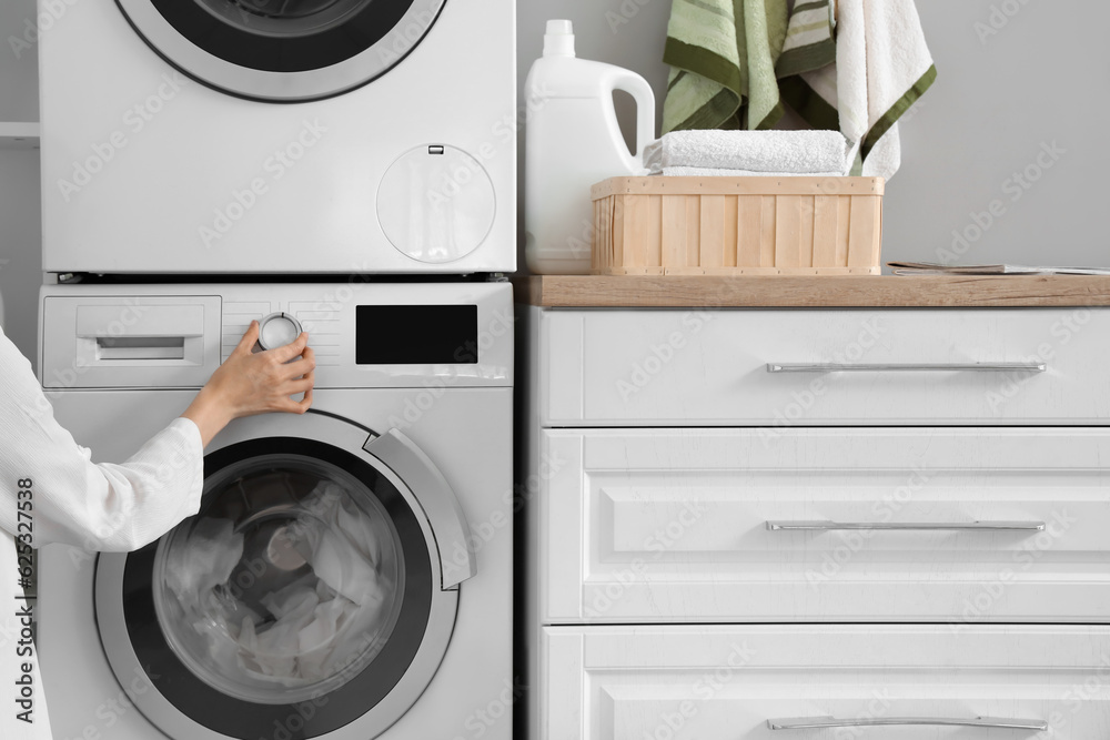 Woman setting up washing machine with dirty clothes in laundry room