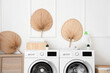 Washing machines with bottle of detergent, towels and houseplants in laundry room
