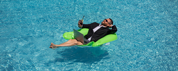 Funny business man in a business suit floating in the water in the pool. Remote summer work online. Crazy freelancer. Business and summer. Business man drink summer cocktail and using laptop in pool.