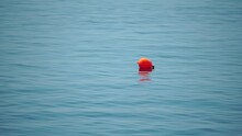 Orange Buoy Floating On The Surface Of The Sea Waves, Concept Of Human Life Safety. Orange Safety Buoys On A Rope Floating In The Sea On A Sunny Day, Close Up. Fencing Of The Swimming Area On Beach.