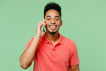 Wall Mural - Young man of African American ethnicity he wear pink t-shirt talk speak on mobile cell phone conducting pleasant conversation isolated on plain pastel light green background studio. Lifestyle concept.