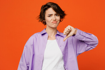 Wall Mural - Young disatisfied upset sad caucasian woman she wear purple shirt white t-shirt casual clothes showing thumb down dislike gesture isolated on plain orange background studio portrait Lifestyle concept