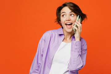 Wall Mural - Young woman she wear purple shirt white t-shirt casual clothes talk speak on mobile cell phone conducting pleasant conversation isolated on plain orange background studio portrait. Lifestyle concept.