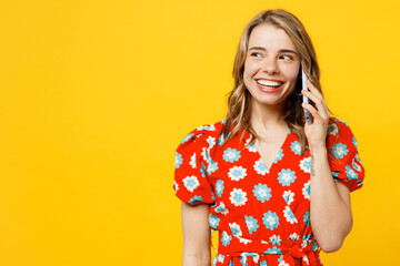 Young smiling caucasian woman she wear red dress casual clothes talk speak on mobile cell phone conducting pleasant conversation isolated on plain yellow background studio portrait. Lifestyle concept.