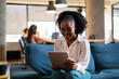 © JustLife - Beautiful African businesswoman sitting on sofa in office. Young woman using digital tablet.