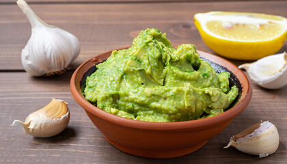 Wall Mural - Clay bowl with fresh guacamole, lemon and garlic on wooden table. Diet vegetarian Mexican food avocado.