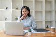 © Natee Meepian - Young happy professional business woman working on laptop in office sitting at desk, business female portrait at workplace