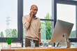 © LIGHTFIELD STUDIOS - myasthenia gravis, bold african american businessman with ptosis syndrome talking on smartphone and standing with walking cane near monitor, dark skinned office worker, inclusion