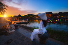Vietnamese Women In National Costumes Sitting Beautiful Night View At The Ancient Town. Vietnam. Hoi An. Street View With Traditional Boats And Lifestyle On The Background Of The Ancient Town.