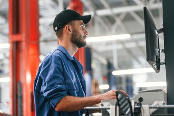 In black cap. Using computer. Auto mechanic working in garage. Repair service