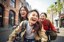Happy Group Of Young Japanese People With Backpack Riding A Bike In Amsterdam. Life Style Concept With Friends Having Fun Together On Summer Holiday