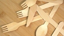 Wooden Eco-friendly Disposable Tableware Falling On The Table. Pile Of Wooden Spoons, Forks And Knives On Cutting Board Surface. Disposable Ecological Tableware For Kitchen And Restaurant