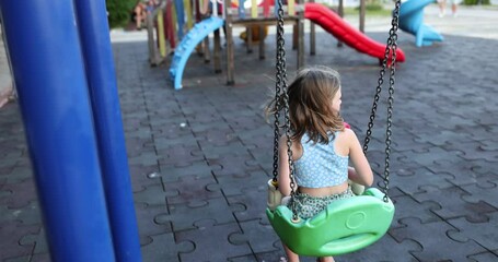 little girl rides on swing against children slide on modern playground at daytime. concept of entert