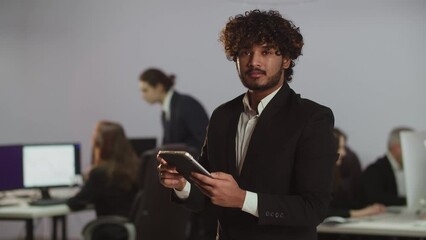 Wall Mural - A young man in a business suit is tapping and scrolling across the digital tablet screen. A young entrepreneur checks company reports on his digital tablet.