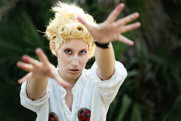 Italian girl cosplay Giorno Giovanna from the anime jojo. Blond woman with blue eyes. Close up to the sea and greenery.