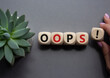 Oops symbol. Concept word Oops on wooden cubes. Businessman hand. Beautiful grey background with succulent plant. Business and Oops concept. Copy space.