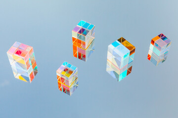 Glass geometric prism cubes with light diffraction of rainbow spectrum colors on blue sky mirror reflection. Sun, trendy sunlight and shadows. Overhead view, flat lay. Creative summer idea.