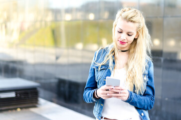 Wall Mural - happy blonde young woman outdoor using her mobile phone isolated