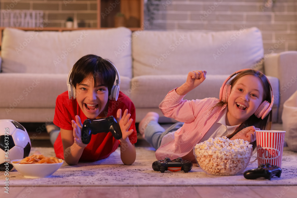 Little children playing video game at home in evening