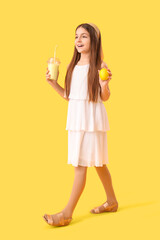 Wall Mural - Little girl with glass of smoothie and lemon on yellow background