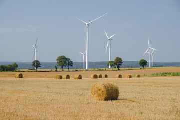 Green energy and agriculture: field with heaps of hay and wind turbines