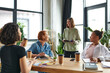 © LIGHTFIELD STUDIOS - young and pleased woman standing with notebook near smiling multiethnic female friends sitting at table with coffee to go in women interest club, mutual support and understanding concept