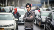© wetzkaz - stands as a pedestrian in the middle of a traffic jam, neutral facial expression to almost serious, young adult man with glasses and wearing sweater and shirt, Asian, fictional place