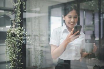 Wall Mural - Attractive young woman talking on the smart phone and smiling while standing in office and looking smart phone.