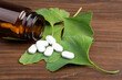 Bottle of pills and fresh ginkgo biloba leaves on wooden background. Traditional, herbal medicine and Homeopathy concept.
