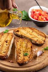 Wall Mural - Pouring oil onto slice of toasted bread ready to make toasts. Food recipe background. Close up